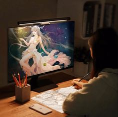 a woman sitting at a desk in front of a tv with anime artwork on it