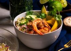 a white bowl filled with shrimp and vegetables next to a glass of limeade on a table