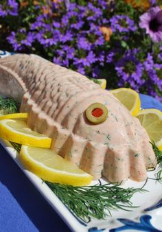 a fish made out of lemons and dill on a plate with purple flowers in the background