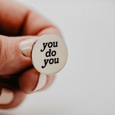 a person holding a button with the words you do you written on it in black ink