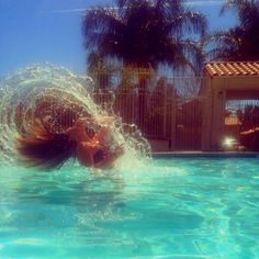 a woman is swimming in the pool with her hair blowing back and legs spread out