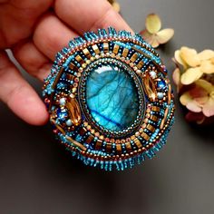 a person holding a brooch in their hand with beads and stones around it on a table