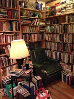 a room filled with lots of books and a green chair in front of a lamp