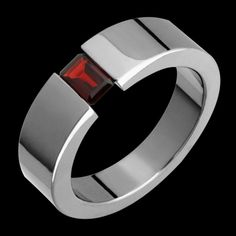 a silver ring with a red stone in the center on a black background, close up