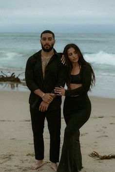 a man and woman standing on top of a sandy beach next to the ocean,