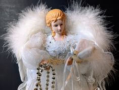 an angel doll holding a teddy bear in her arms with pearls and beads around it