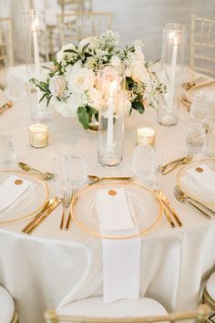 the table is set with white and gold plates, silverware, and flowers in vases