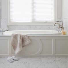 a white bath tub sitting under a window next to a pair of slip on shoes