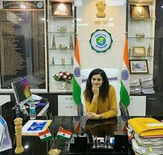 a woman sitting at a desk in an office with many flags on the wall behind her