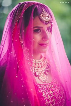 a woman wearing a pink veil and jewelry is posing for a photo in her wedding outfit