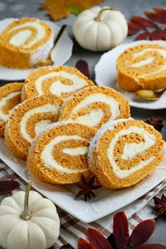 several pumpkin rolls are on plates next to small white pumpkins and anisette