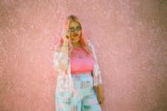 a woman standing in front of a pink wall talking on a cell phone