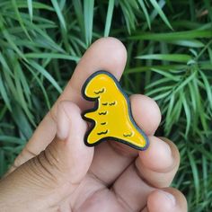 a hand holding a yellow and black brooch in front of some green grass,