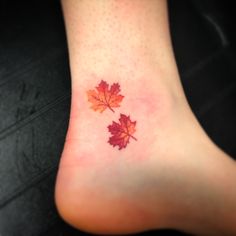 a small leaf tattoo on the foot of a woman's feet, with red leaves