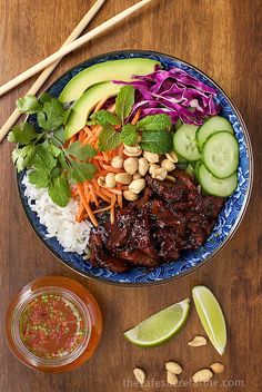 a blue plate topped with meat and veggies next to chopsticks on top of a wooden table