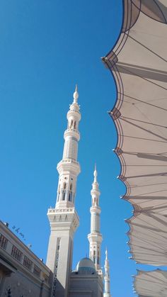 two tall white buildings sitting next to each other on a blue sky day with an open umbrella over them