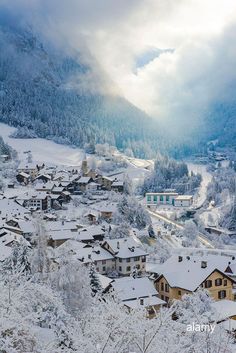 the snow covered village is surrounded by mountains and trees, with houses in the foreground