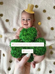 a person holding a baby in front of a fake broccoli plant with a gold top hat