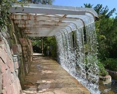 a stone walkway with water casing over it and trees in the backround