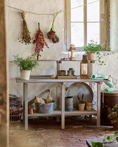 pots and pans are hanging on the wall next to a table with plants in it