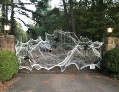 a spider web covered gate in front of some trees and bushes with lights on it