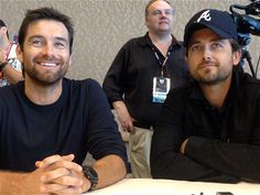 two men sitting at a table with cameras behind them