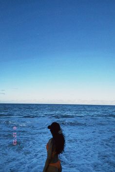 a woman is standing in the water with her back to the camera and looking at the sky