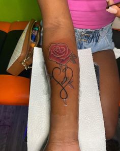 a woman's arm with a rose and two hearts tattooed on the left forearm