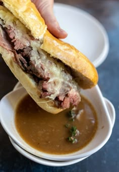 a hand holding a sandwich over a bowl of soup