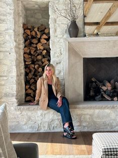 a woman sitting in front of a fire place with logs on the wall behind her