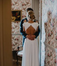 a bride and groom standing in front of a floral wallpapered room looking at each other