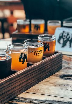 several glasses of beer are sitting on a tray in front of a sign that says california coast