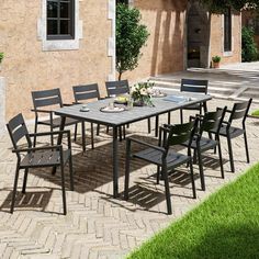 an outdoor dining table and chairs set up in front of a brick building with green grass