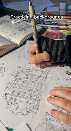 a person is drawing on some paper with a pencil and pen in their hand while sitting at a desk full of books