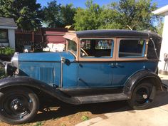 an old blue car parked in front of a house