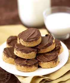 chocolate covered cookies on a white plate next to a glass of milk and napkins