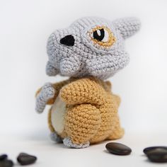 a crocheted stuffed animal sitting on top of a pile of black rocks next to it's eyes