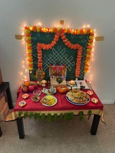 a red table topped with plates of food next to a chalk board covered in lights