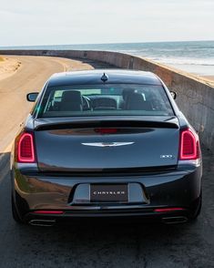 the back end of a black car parked on the side of the road next to the ocean