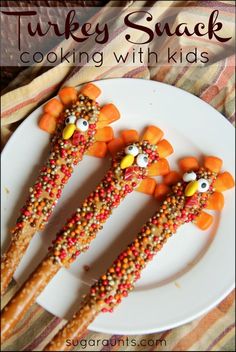 three sticks decorated like turkeys and carrots on a white plate with candy sprinkles