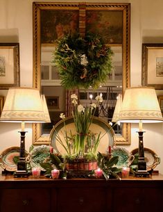 a table with two lamps on top of it next to a mirror and pictures in the background