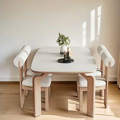 a white table with four chairs and a small vase on top of it in front of a window