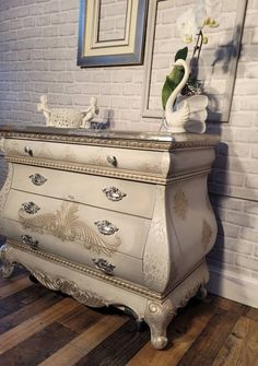 a white dresser sitting on top of a hard wood floor next to a brick wall