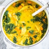 a white bowl filled with chicken and spinach soup on top of a marble counter