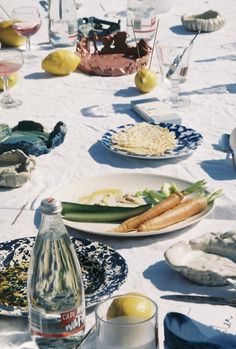 a table topped with plates and bowls filled with food next to bottles of wine, glasses and lemons