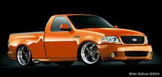 an orange pick up truck parked in front of a black background with the hood down