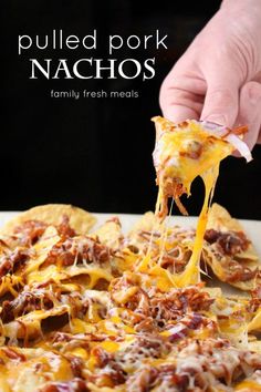 a person is taking a slice of pulled pork nachos from a white plate