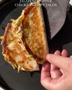 a person is holding up a piece of food on a black plate with the words jalapeno popper chicken crispy tacos