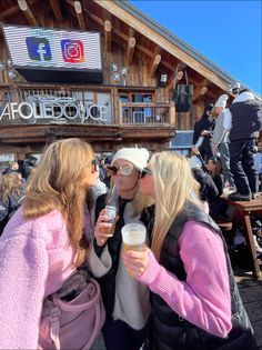 three women are standing together and drinking coffee at a ski lodge in the mountains,