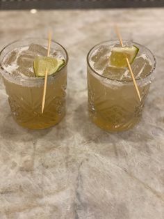 two glasses filled with drinks sitting on top of a marble counter next to each other